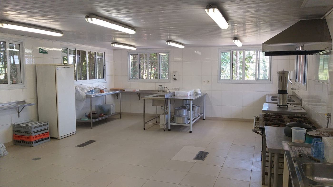 Outro ângulo da cozinha industrial, com bancadas de inox, coifa e geladeira