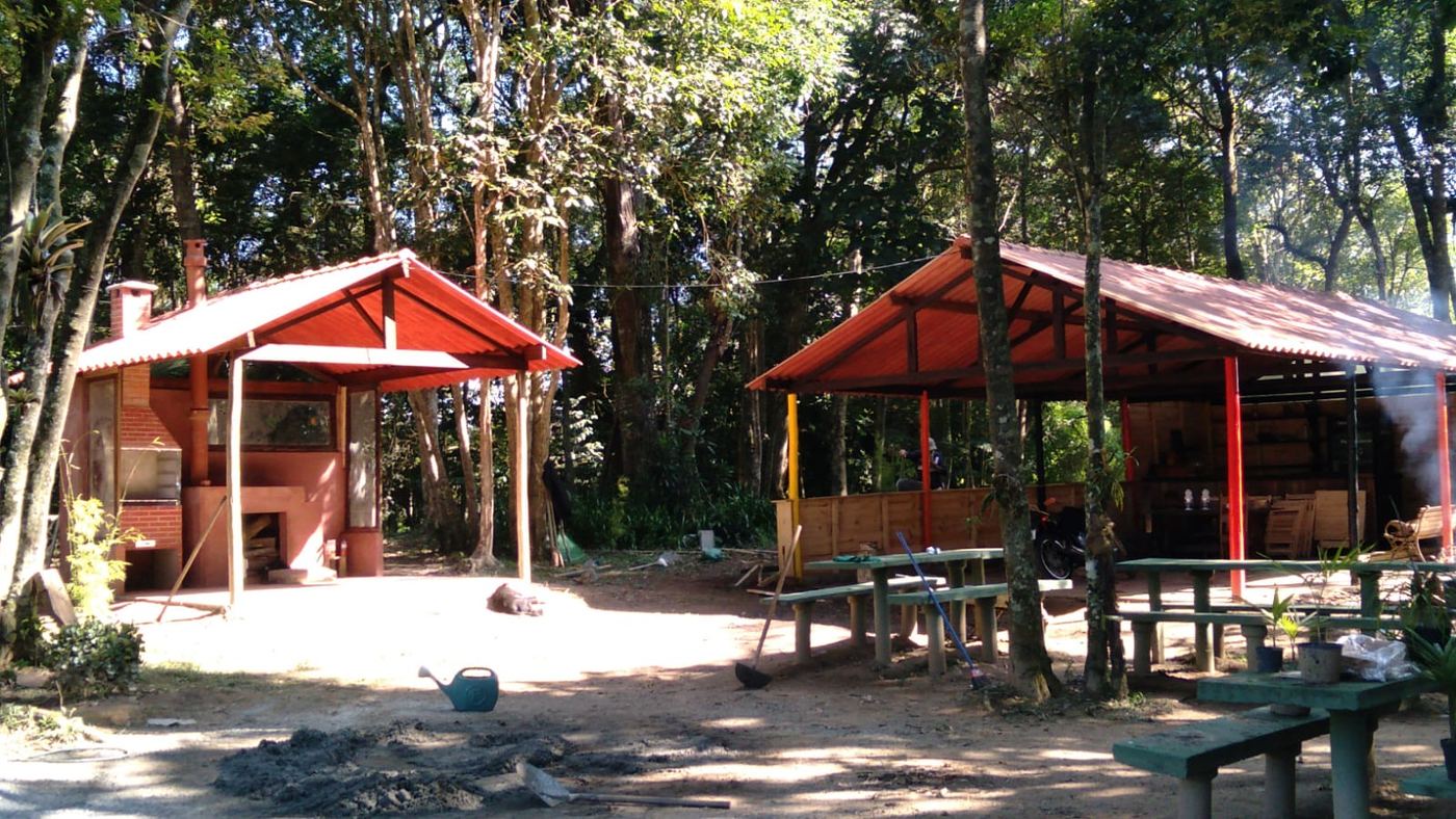 Dois quiosques de telha vermelha com mesas, entre árvores